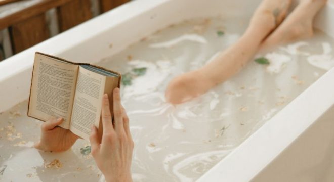 A woman reads. a book while soaking in an herbal bath