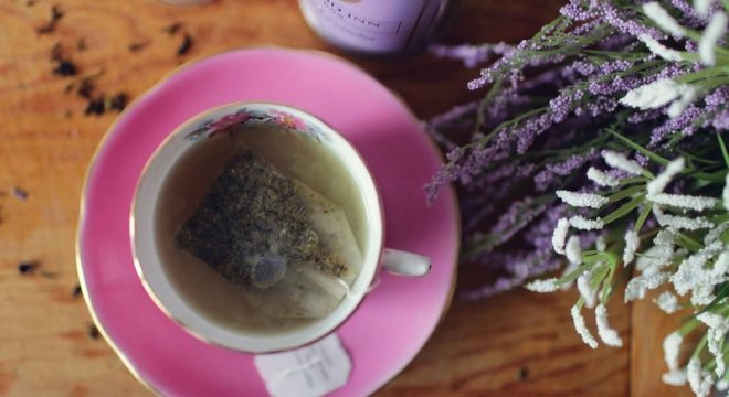 A-teacup-with-a-teabag-full-of-natural-components-sits-next-to-a-cluster-of-flowers-