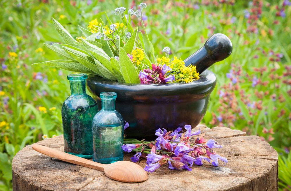 black mortar with healing herbs and sage, glass bottle of essential oil outdoors
