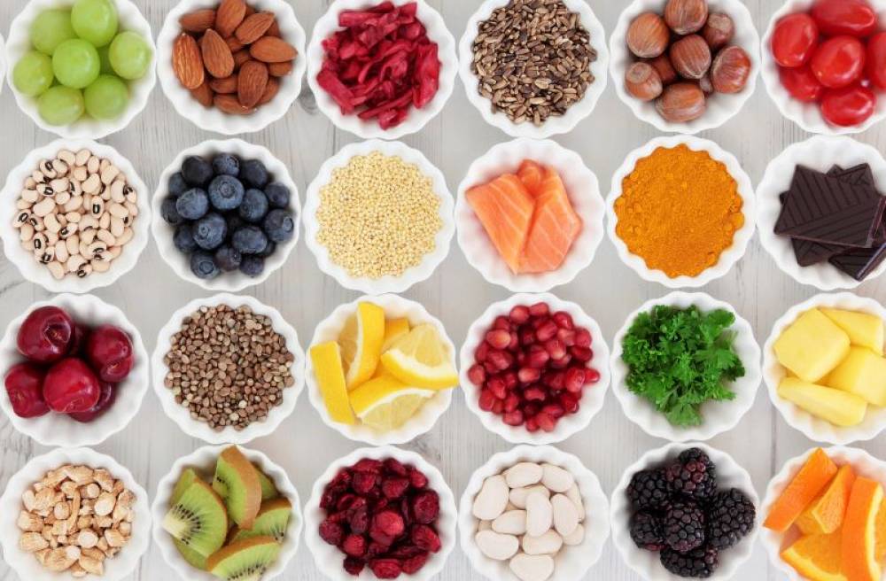 Assortment of nutrient-rich foods including berries, nuts, seeds, beans, salmon, citrus, leafy greens, turmeric, and dark chocolate in small bowls.