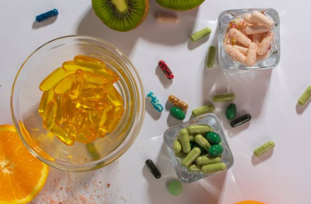 Fish oil softgels, vitamin capsules, and fresh fruit arranged on a tabletop, illustrating dietary supplements and nutrition.