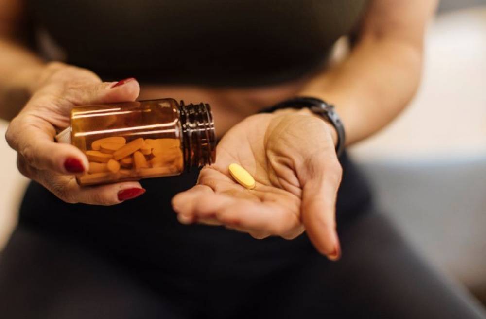 Person holding a bottle of dietary supplements and placing a yellow tablet into their hand.