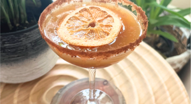 Apple Mock-tini in a glass on a table with green plants behind it