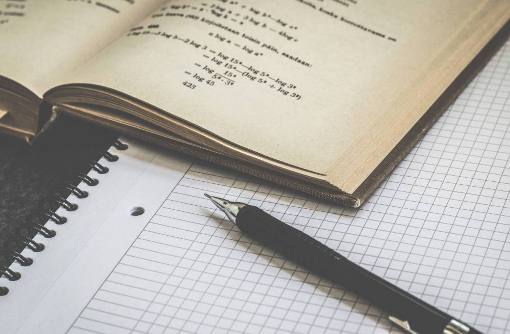 Open textbook showing logarithm equations next to a spiral notebook with graph paper and a pen