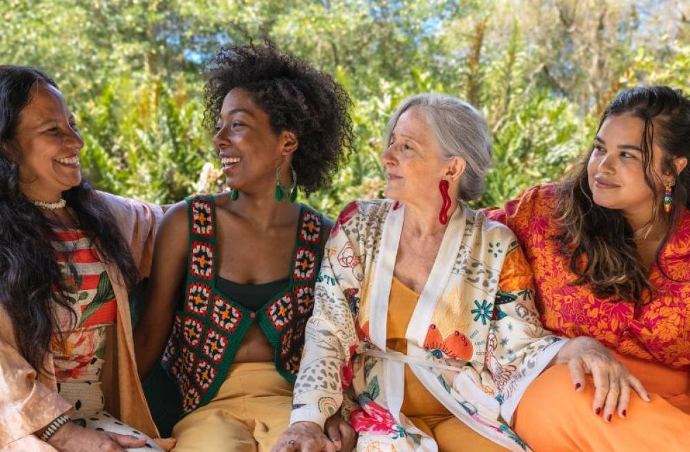 Four diverse women of different ages and backgrounds smiling together outdoors.