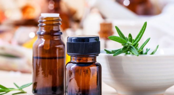 Bottles of essential oils next to a white bowl with green herbs