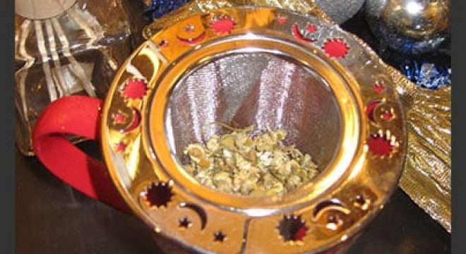 dry camomile tea sits in a tea strainer, ready for hot water to be poured over it into the cup below