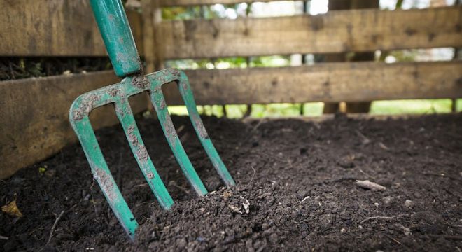 35893240 - garden fork turning black composted soil in wooden compost bin