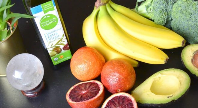 fruits and veggies are laid out on a dark table, including bananas, avocado and broccoli