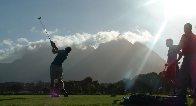 three people are on a golf course, one of them is swinging their club while the other two stand off to the side watching