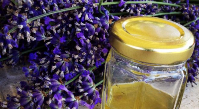 lavender flowers sit on a table behind a small jar of honey-like liquid