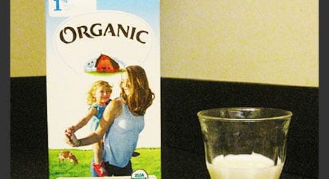 container of milk saying "organic" on it sits on a table next to a clear glass halfway filled with milk