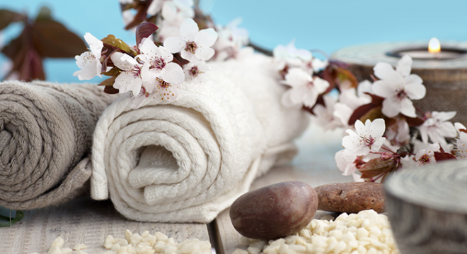 spa towels are rolled up and displayed on a table with white flowers and candles